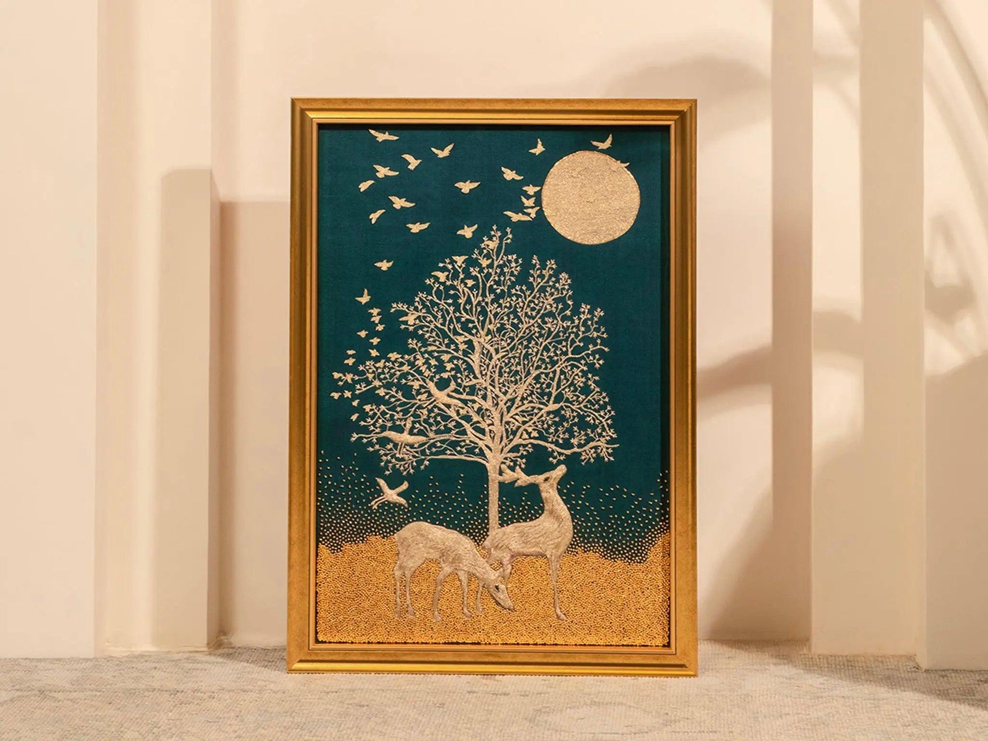 A framed embroidery artwork featuring a golden tree of life with deer, birds, and a moon in a night sky setting.