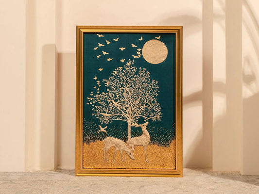 A framed embroidery artwork featuring a golden tree of life with deer, birds, and a moon in a night sky setting.