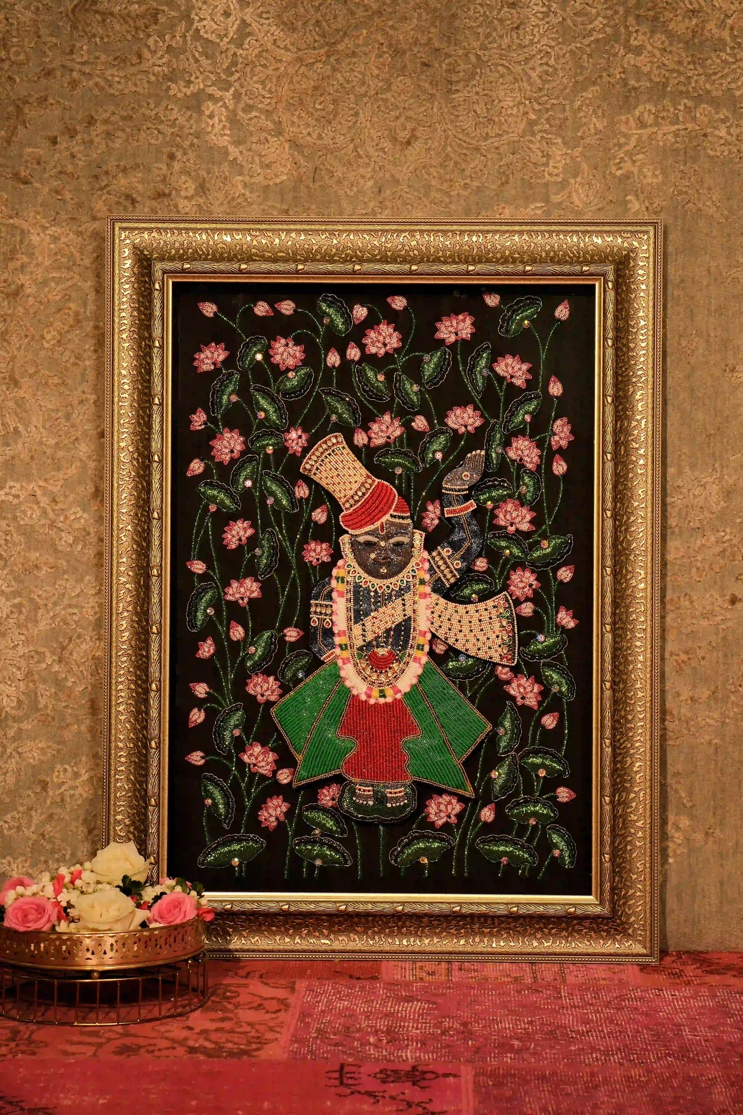 Luxury hand embroidery of a figure with floral motifs in a gold frame on textured wall