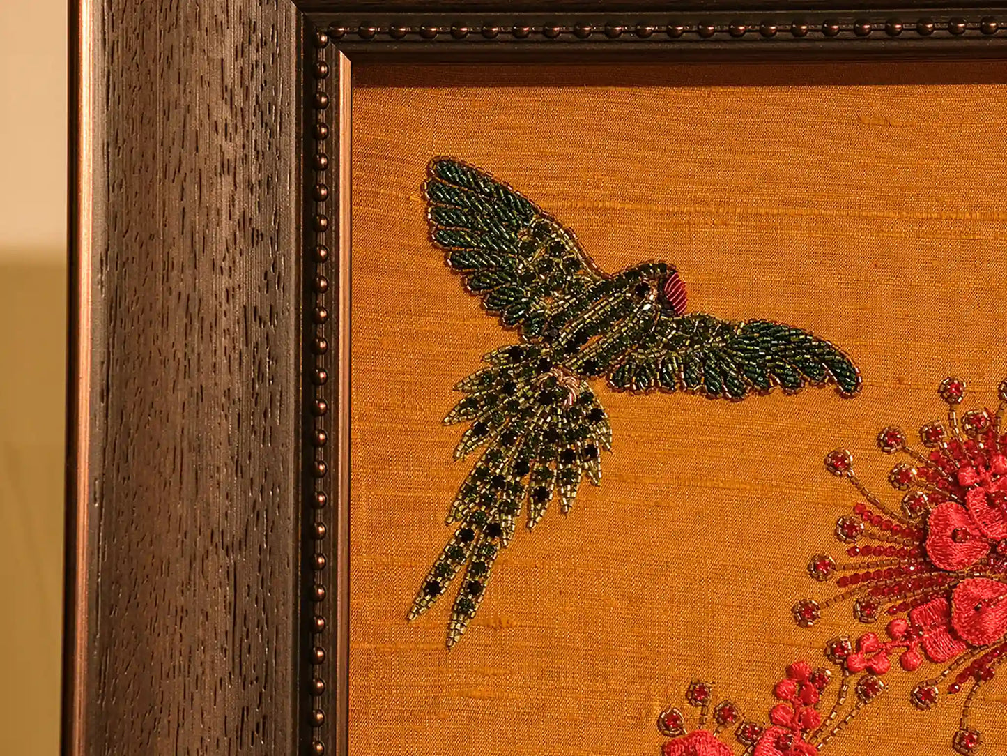 Embroidered artwork of a hummingbird and flowers on orange fabric with a wooden frame.