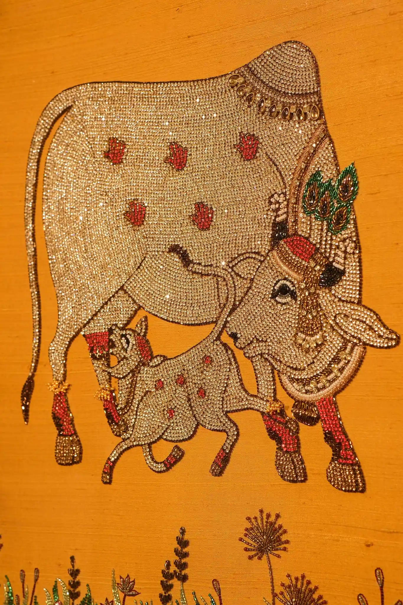 Decorative depiction of a cow and calf with intricate beadwork on an orange background