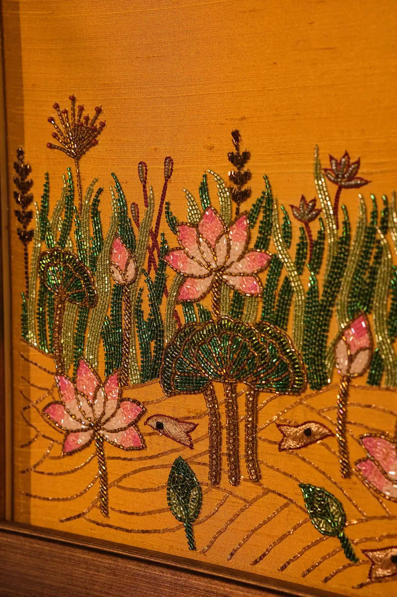 Embroidered design of pink flowers and green leaves on a wooden surface