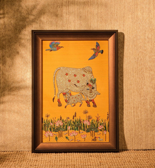 Framed artwork of a cow and birds on a yellow background, leaning against a textured brown wall.