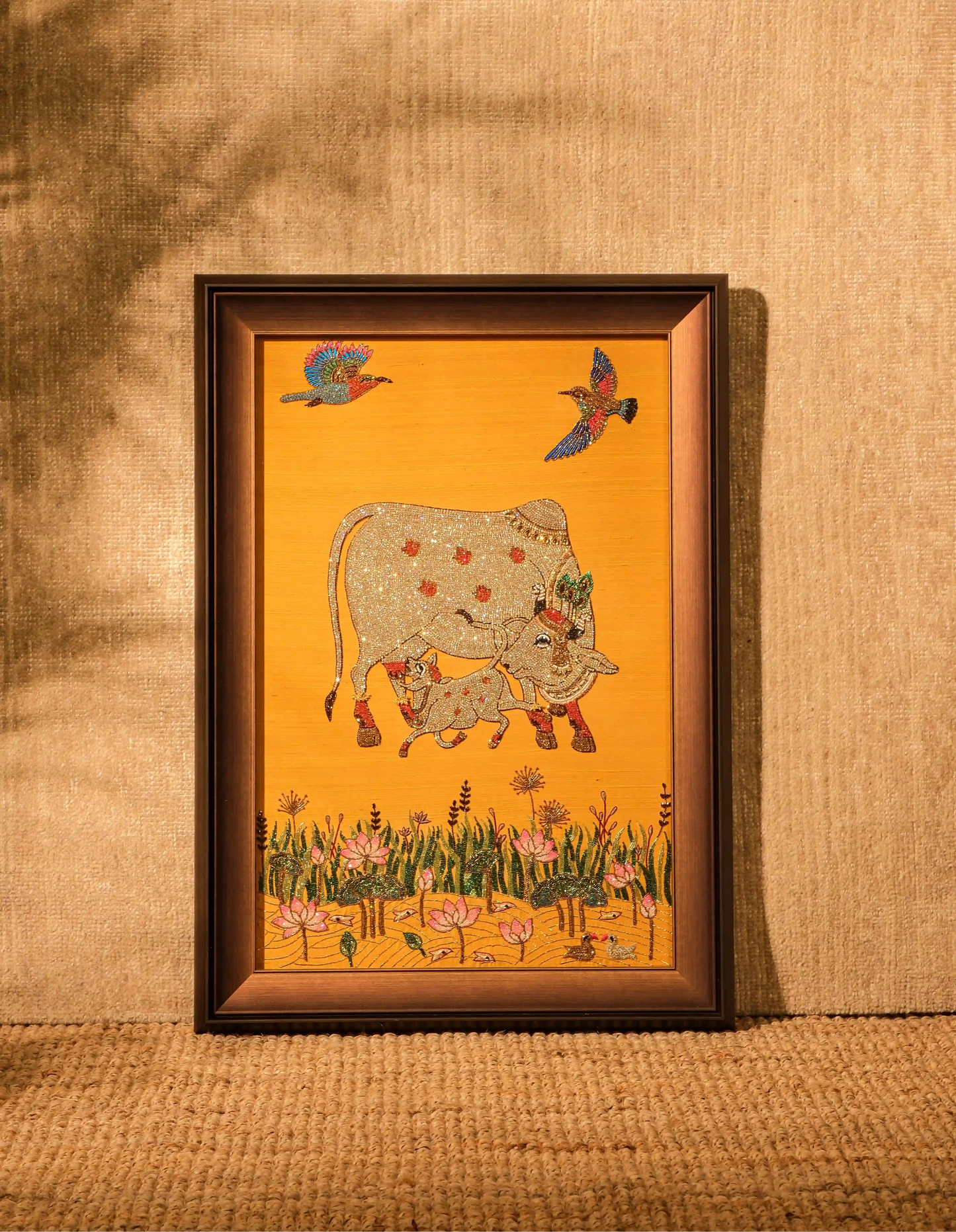 Framed artwork of a cow and birds on a yellow background, displayed on a textured wall.