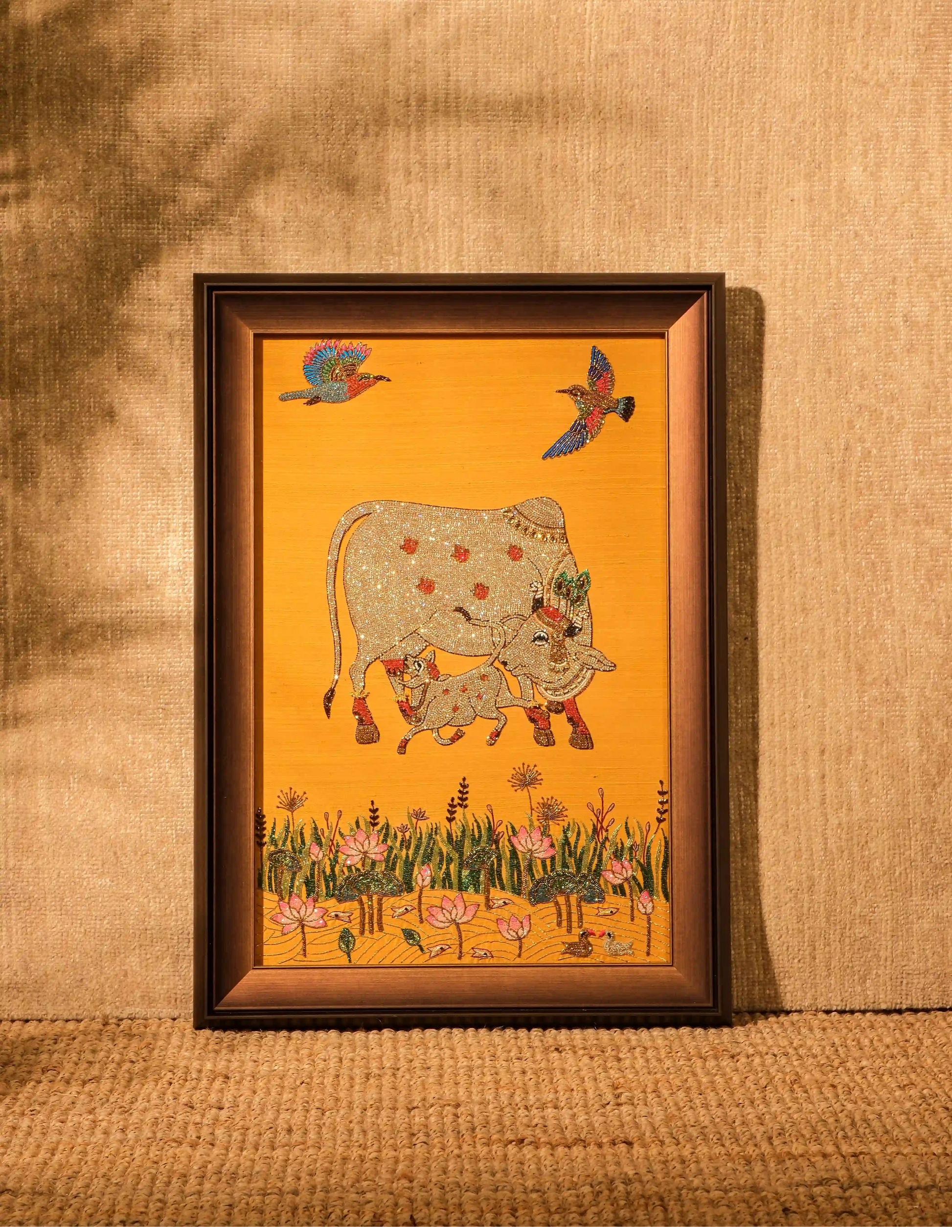 Framed artwork of a cow and birds on a yellow background, displayed on a textured wall.
