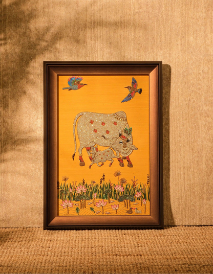 Framed artwork of a cow and birds on a yellow background, displayed on a textured wall.